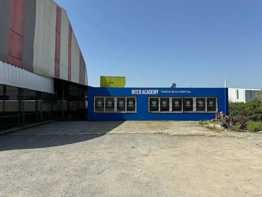Tesisin dış girişi: mavi cepheli bina ve önünde geniş açık alan.